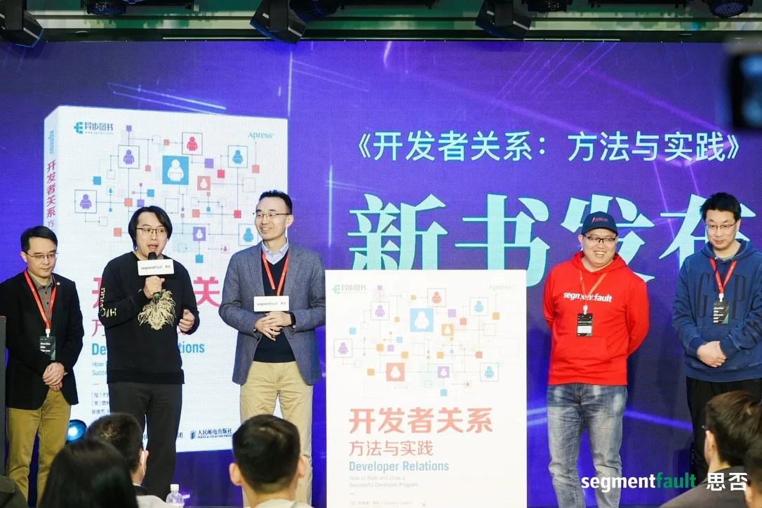 Five people on stage at the Chinese launch of Developer Relations in March 2023, standing beside a large standee of the book cover; I am second from the left, holding a microphone.