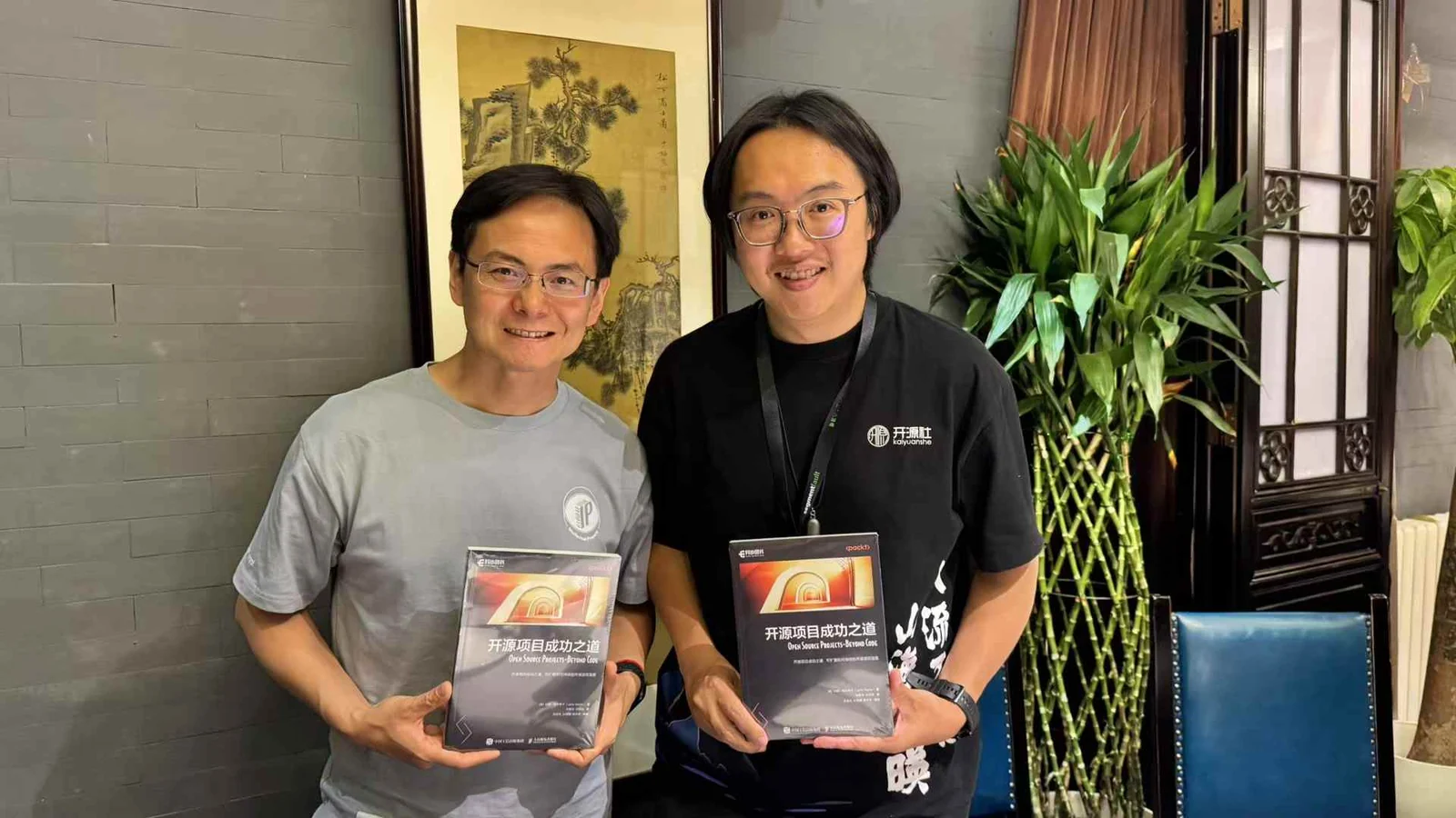 Two of us standing side by side, each holding a shrink-wrapped copy of the Chinese edition of Open Source Projects – Beyond Code.