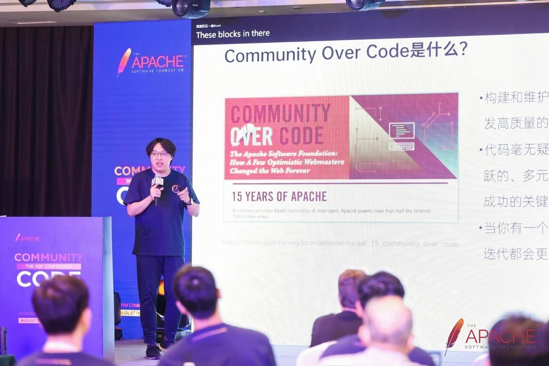 Speaking alone on stage at CommunityOverCode Asia 2023, microphone in hand, in front of a slide asking what Community Over Code means.